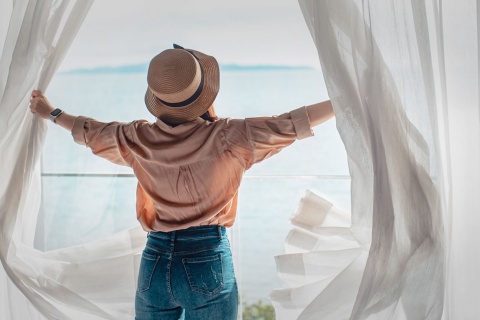 Turista abrindo as cortinas do seu quarto de hotel