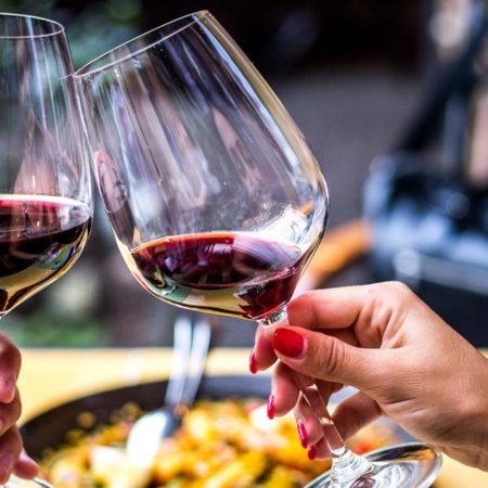 Toasting with red wine and a paella in the background