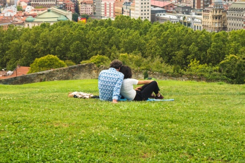 Couple watching a beautiful panoramic view of the city sitting in the park, on the hill above the Old Town