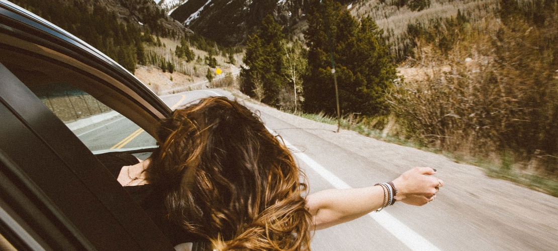 Chica se asoma por la ventanilla de un coche en una carretera de montaña