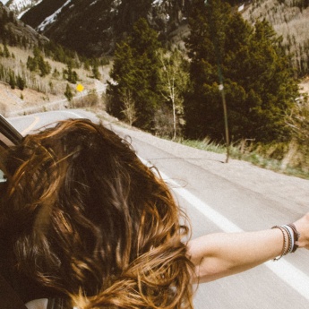 Chica se asoma por la ventanilla de un coche en una carretera de montaña