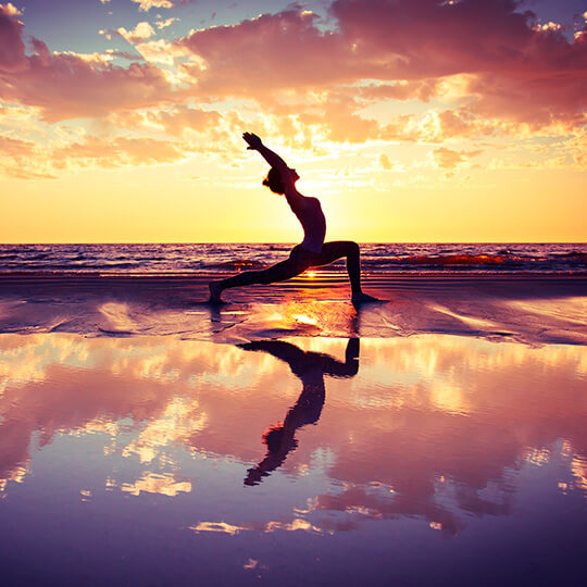 Donna che fa yoga sulla spiaggia al tramonto