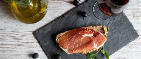 Une tapa de jambon avec de l'huile et un verre de vin rouge 