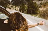 Girl leans out of a car window on a mountain road